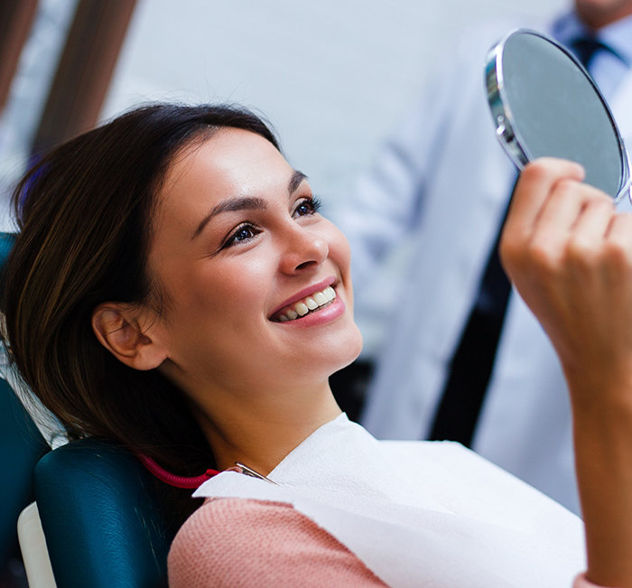 Woman in dental chair looking at her smile in a mirror