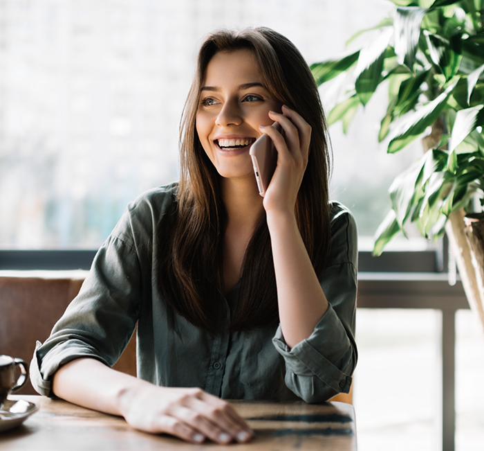 Young woman smiling while talking on the phone with dental office in Brenham