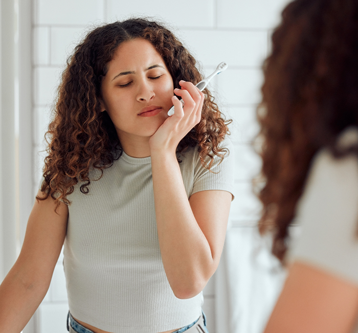 Woman with a toothbrush holding her face in pain before emergency dentistry in Brenham