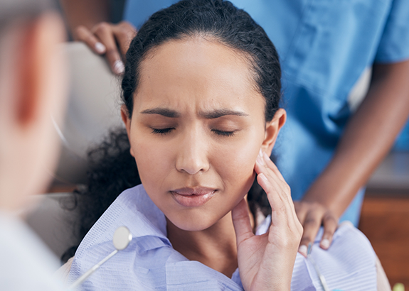 Woman holding her cheek in pain while sitting in dental chair