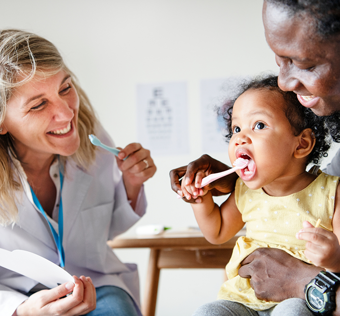 Dentist showing a toddler patient how to brush their teeth