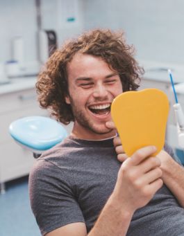 Young man in dental chair looking at his smile in a mirror