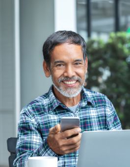 Man in blue plaid shirt smiling and holding his phone