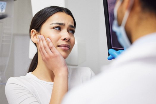 Woman holding hand to face in pain looking at her X-rays with dentist