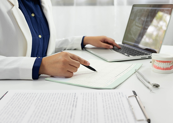 Dentist filling out paperwork while looking at a laptop showing x ray of teeth