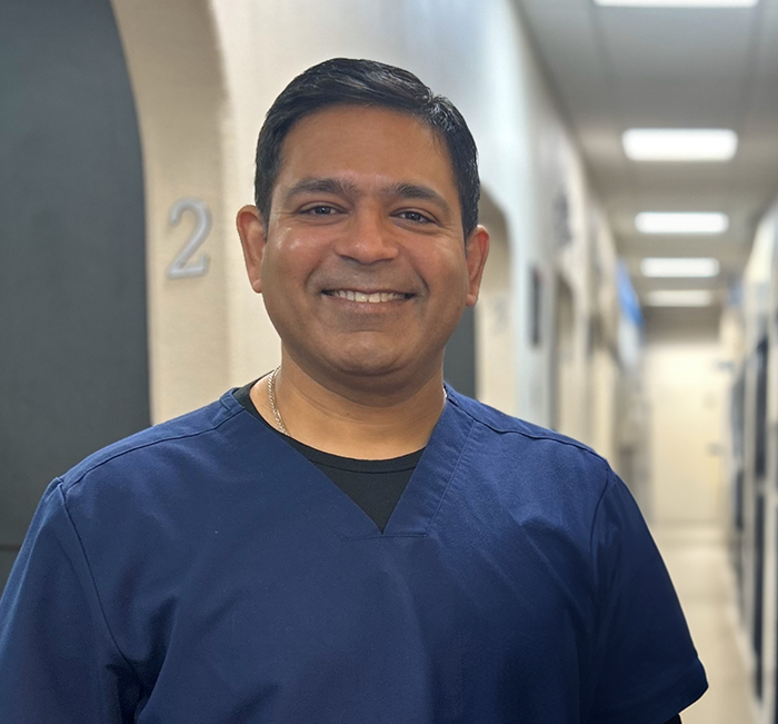 Brenham dentist Doctor Sumeet Sharma smiling in blue scrubs