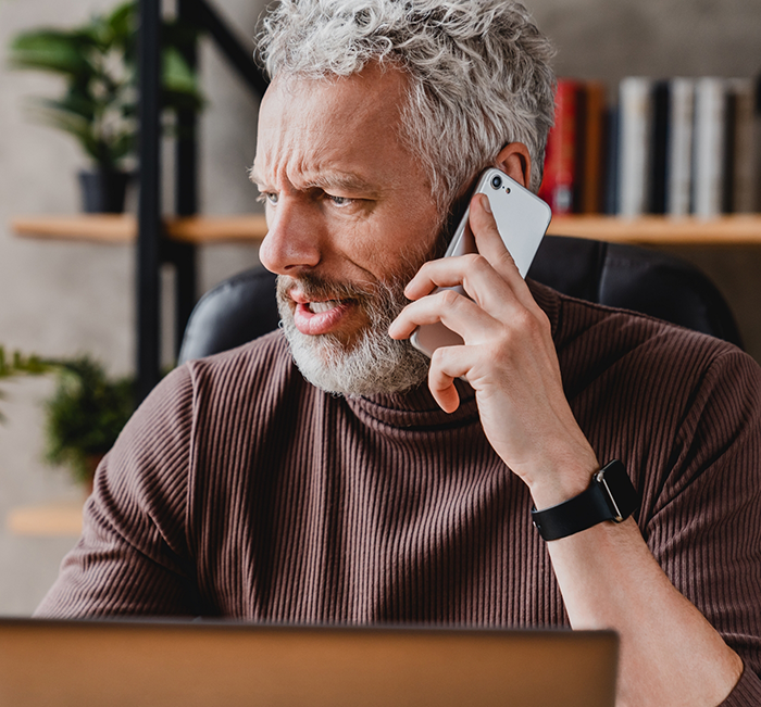 Man with gray hair and beard talking on the phone to request a dental appointment