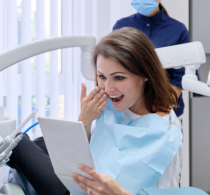 Woman looking at her smile in a mirror after restorative dentistry treatment