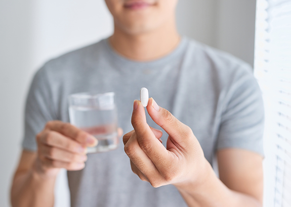 Man holding a white pill and a glass of water