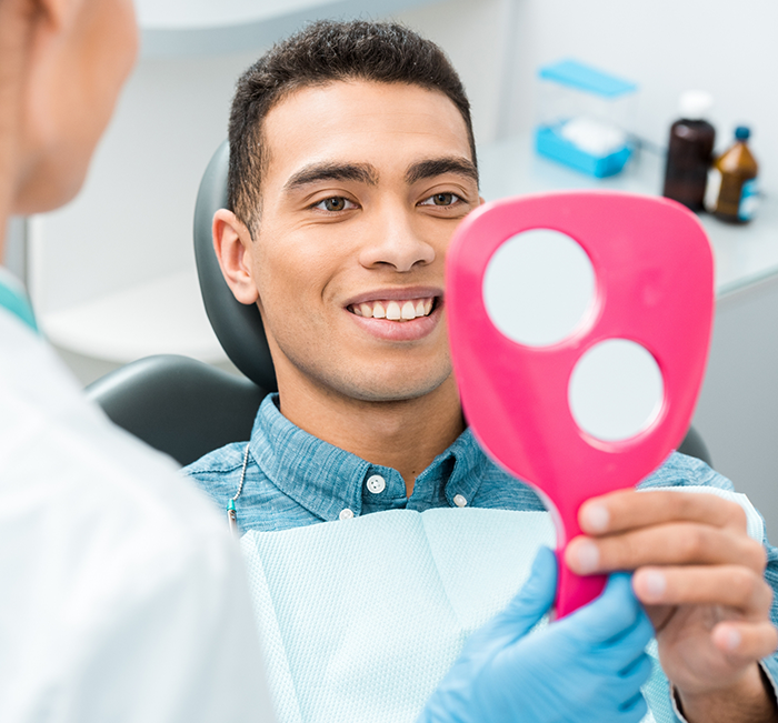 Man in dental chair looking at his smile in a mirror