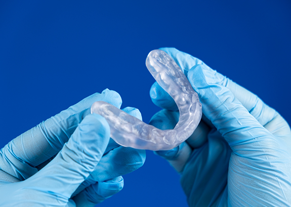 Two gloved hands holding a clear occlusal splint tray