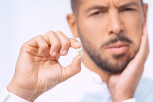 Man holding extracted tooth and touching swollen jaw with hand
